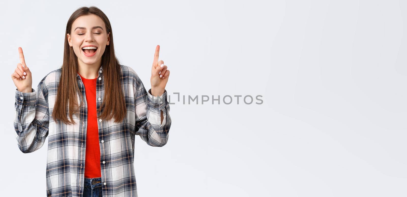 Lifestyle, different emotions, leisure activities concept. Dreamy and happy pretty young woman in checked shirt, dream came true, showing summer vacation resort, pointing fingers up with closed eyes.