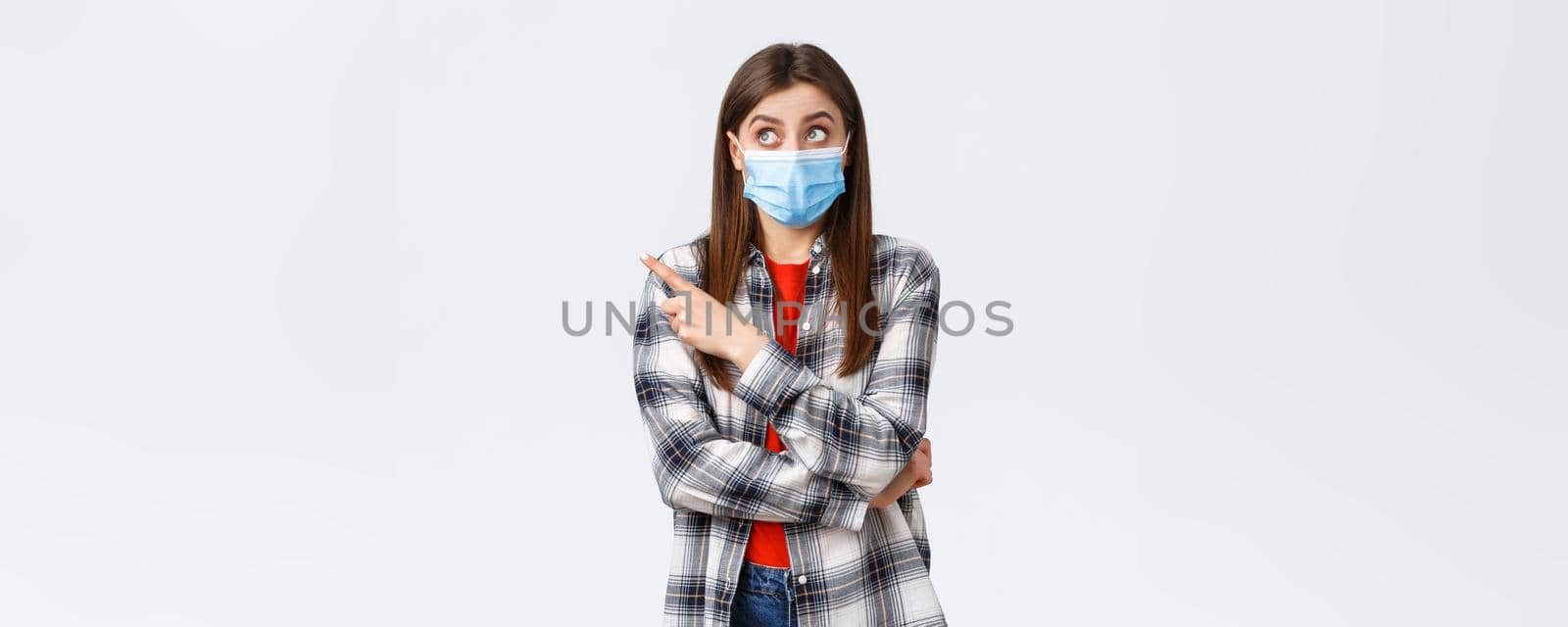 Coronavirus outbreak, leisure on quarantine, social distancing and emotions concept. Intrigued and surprised attractive girl in medical mask, casual clothes, pointing upper left corner interested by Benzoix