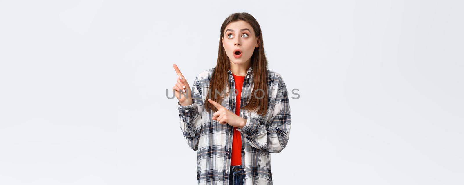 Lifestyle, different emotions, leisure activities concept. Amused attractive girl, european woman in checked shirt pointing and looking upper left corner, captured attention to awesome promo.