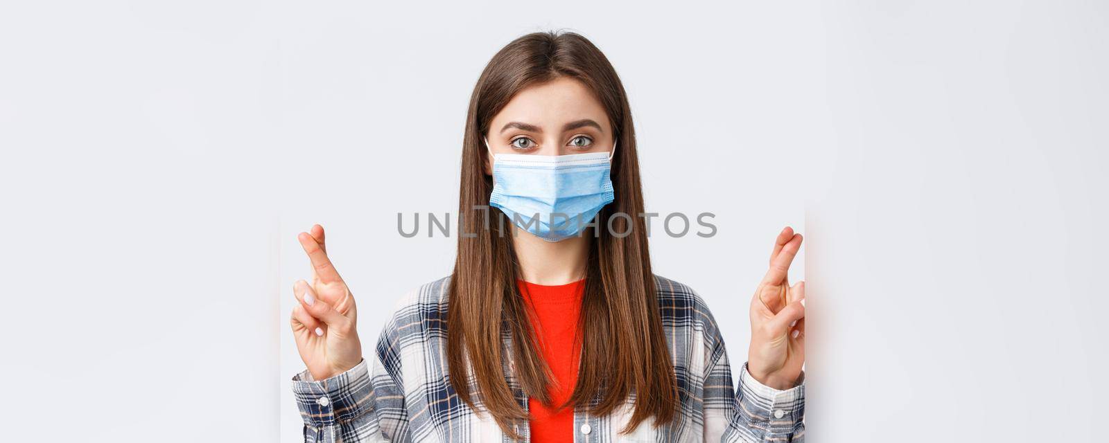 Coronavirus outbreak, leisure on quarantine, social distancing and emotions concept. Close-up of hopeful pretty woman in medical mask, cross fingers good luck, make wish or praying.