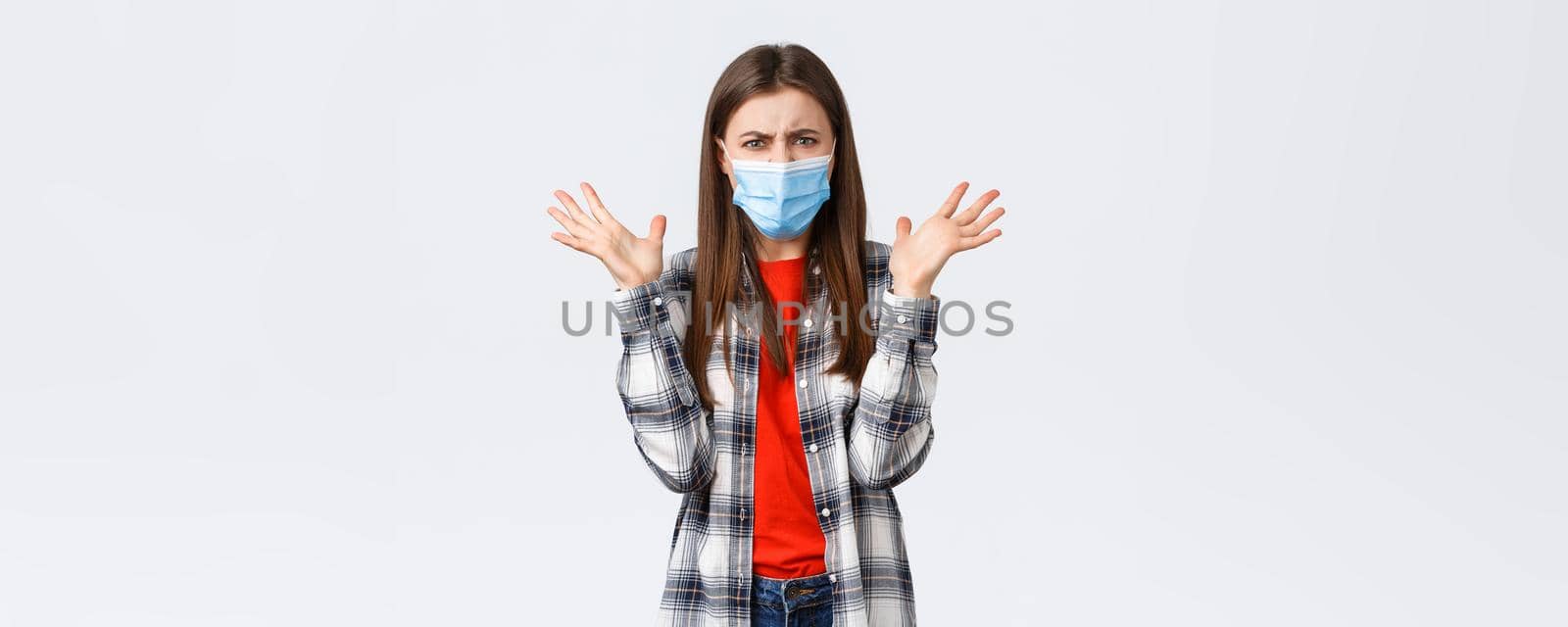 Different emotions, covid-19 pandemic, coronavirus self-quarantine and social distancing concept. Angry, outraged woman in medical mask, arguing, look mad, raise hands in dismay, complaining.