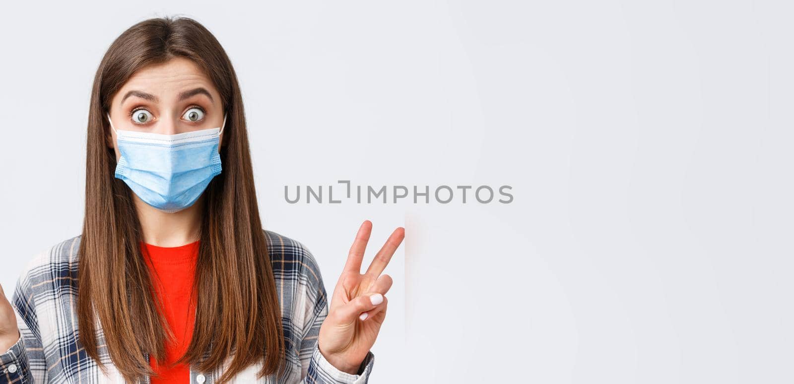 Coronavirus outbreak, leisure on quarantine, social distancing and emotions concept. Close-up of excited and thrilled cute woman in medical mask, showing peace sign or quotes, stare impressed by Benzoix