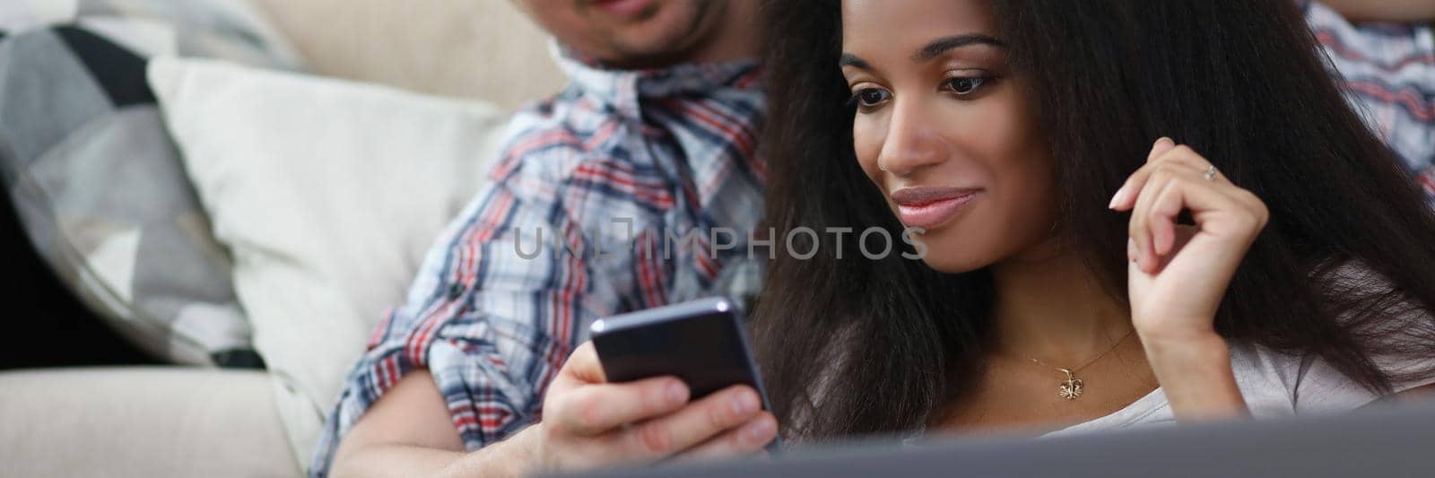 Portrait of middle aged man show content on phone to latin female friend. Woman work from home on laptop. Friends chilling on weekend. Friendship concept