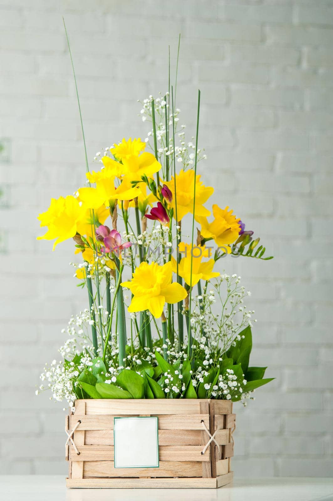 A vertical shot of a beautiful composition with daffodils and pink freesia in a wooden box