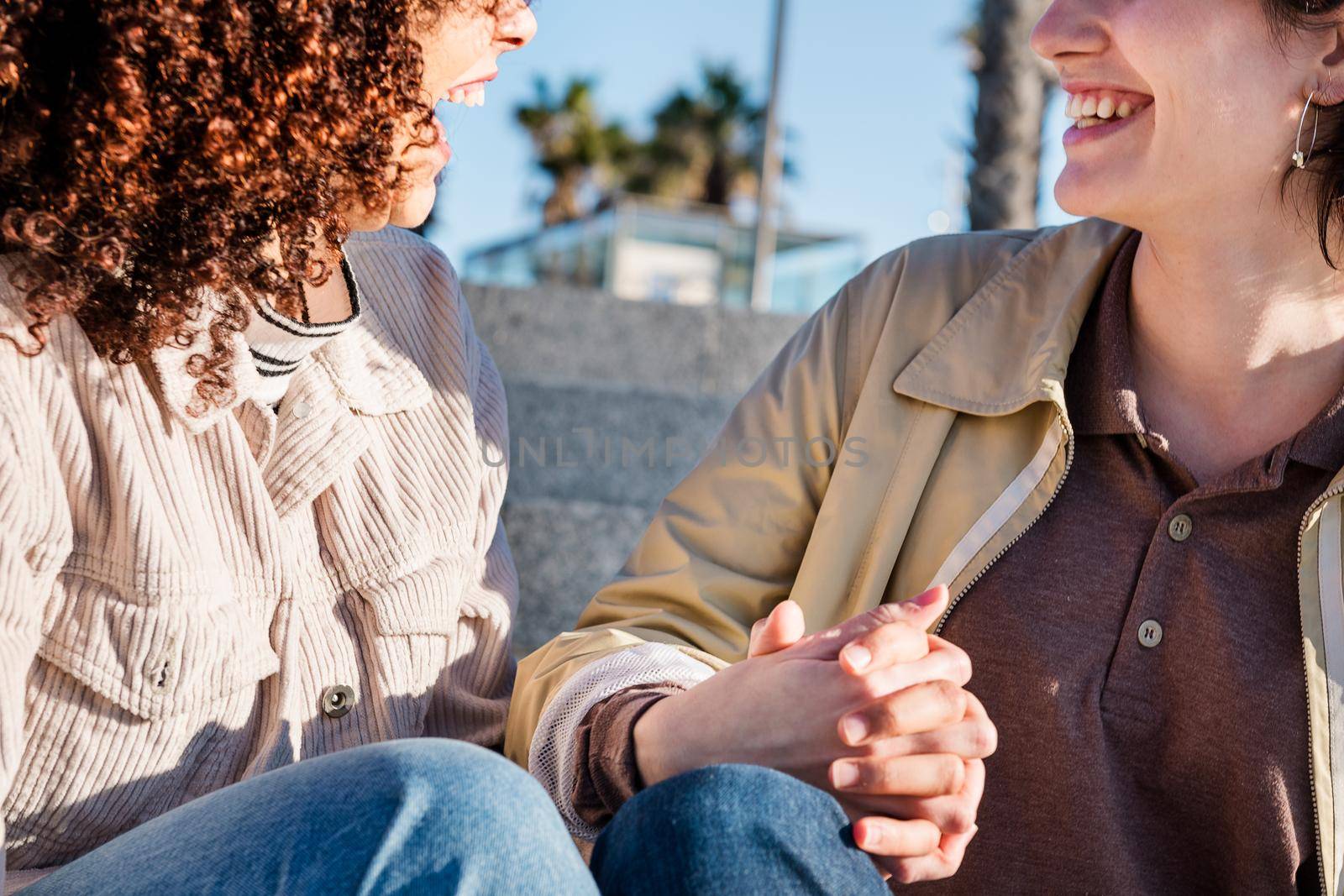 detail of a couple of lesbian women laughing holding hands, concept of sexual freedom and racial diversity