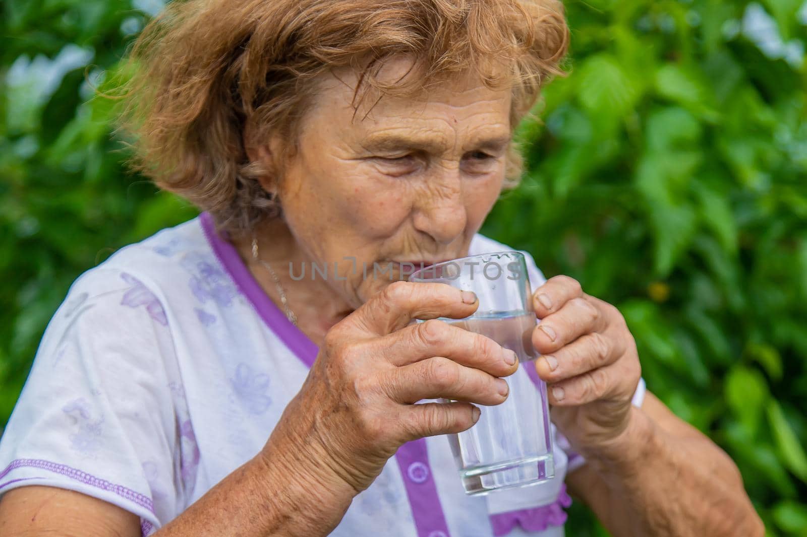 Grandma drinks water from a glass. Selective focus. Woman.