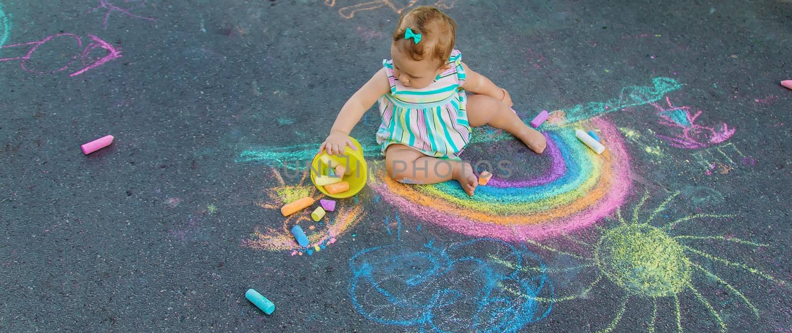 Baby draws a rainbow on the pavement with chalk. Selective focus. Nature.