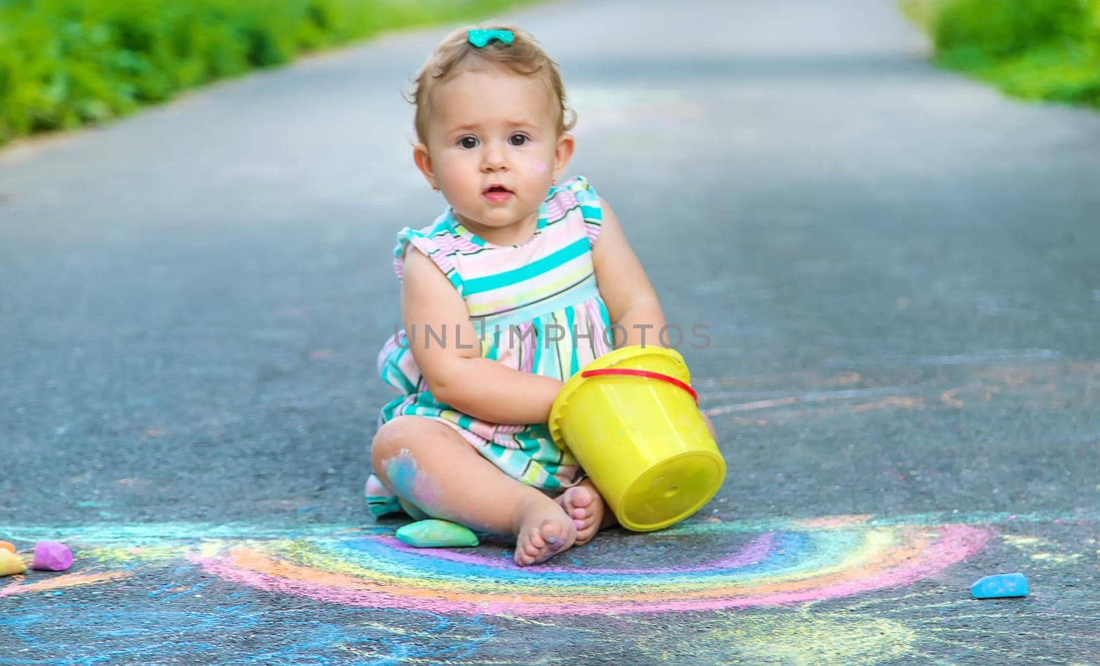 Baby draws a rainbow on the pavement with chalk. Selective focus. Nature.