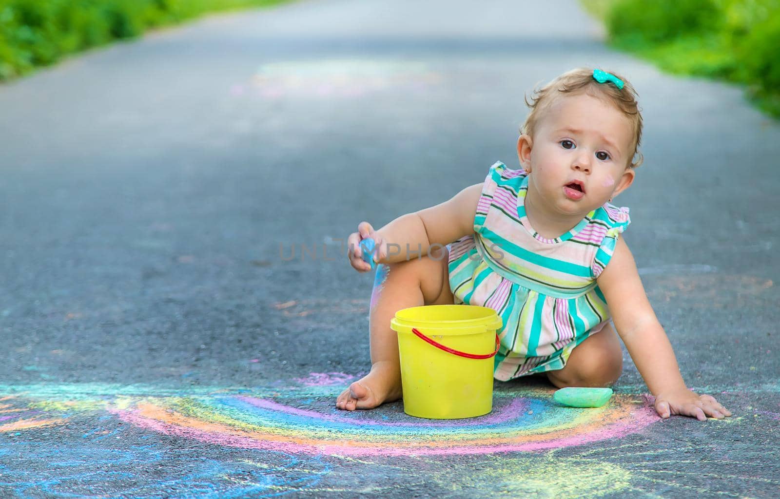 Baby draws a rainbow on the pavement with chalk. Selective focus. Nature.