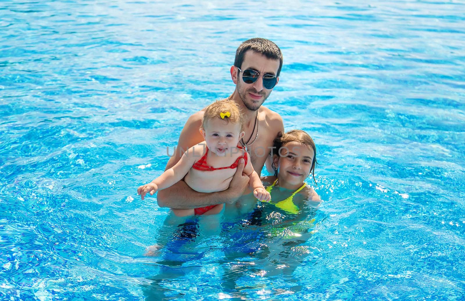 Father with daughters in the pool. Selective focus. by yanadjana