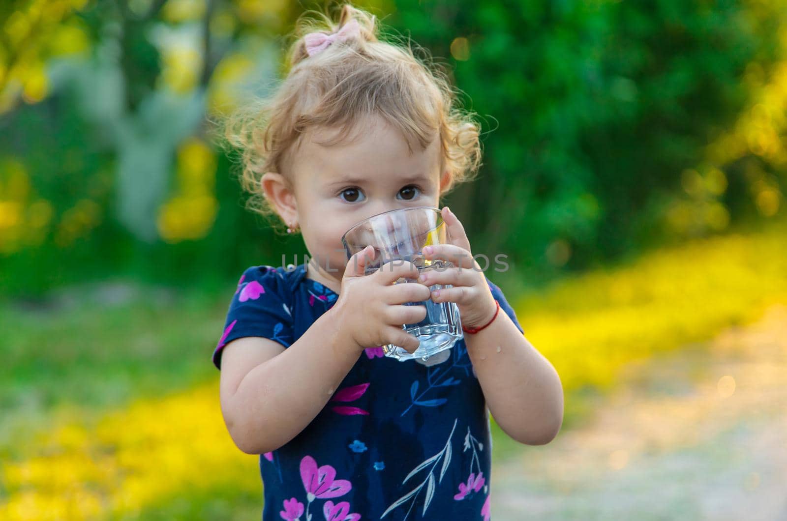 The child drinks water from a glass. Selective focus. Kid.