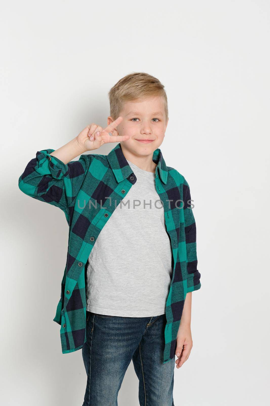 Portrait of cute stylish blond boy kid 7 years old in checked shirt and jeans sitting on a ladder