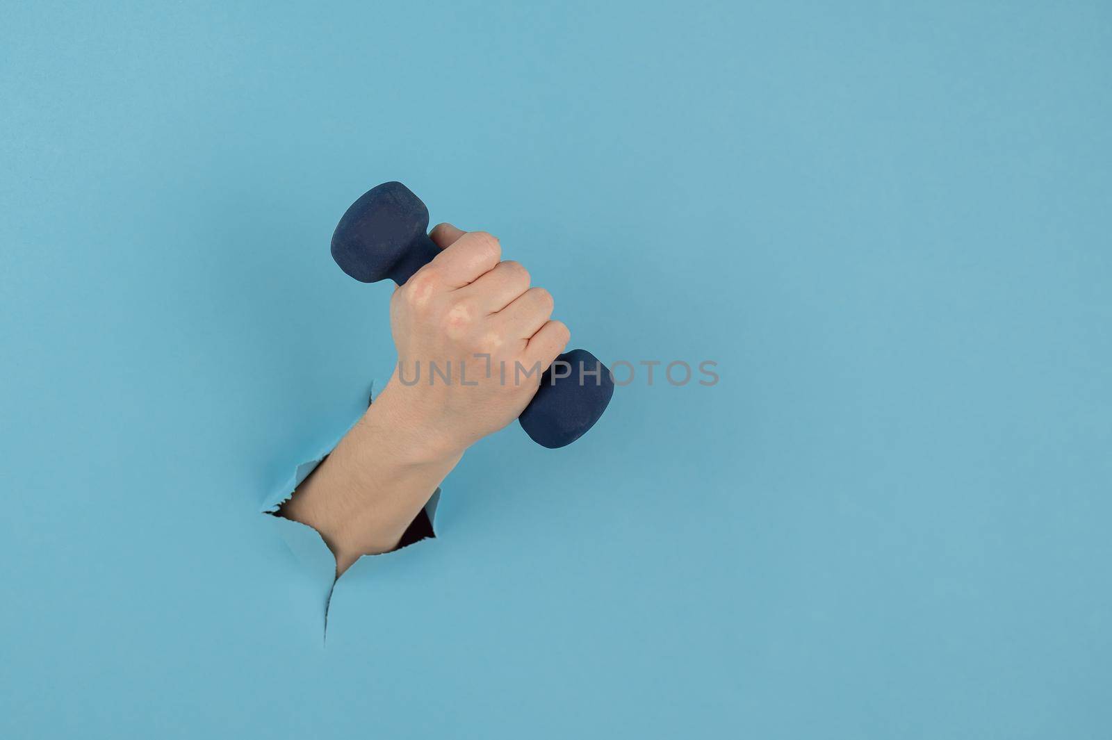 A female hand sticking out of a hole from a blue background holds a dumbbell