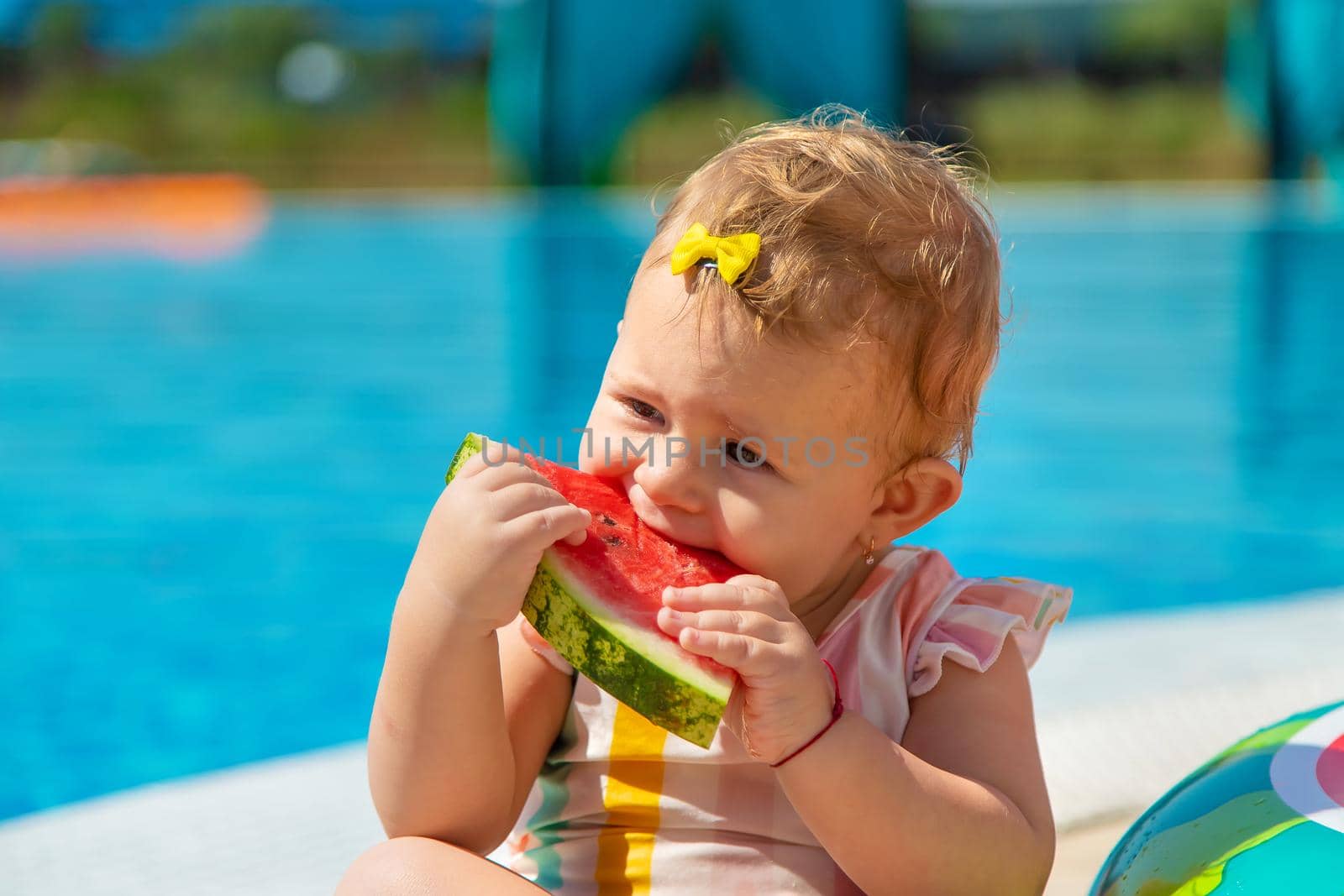 Baby is eating a watermelon by the pool. Selective focus. Kids.