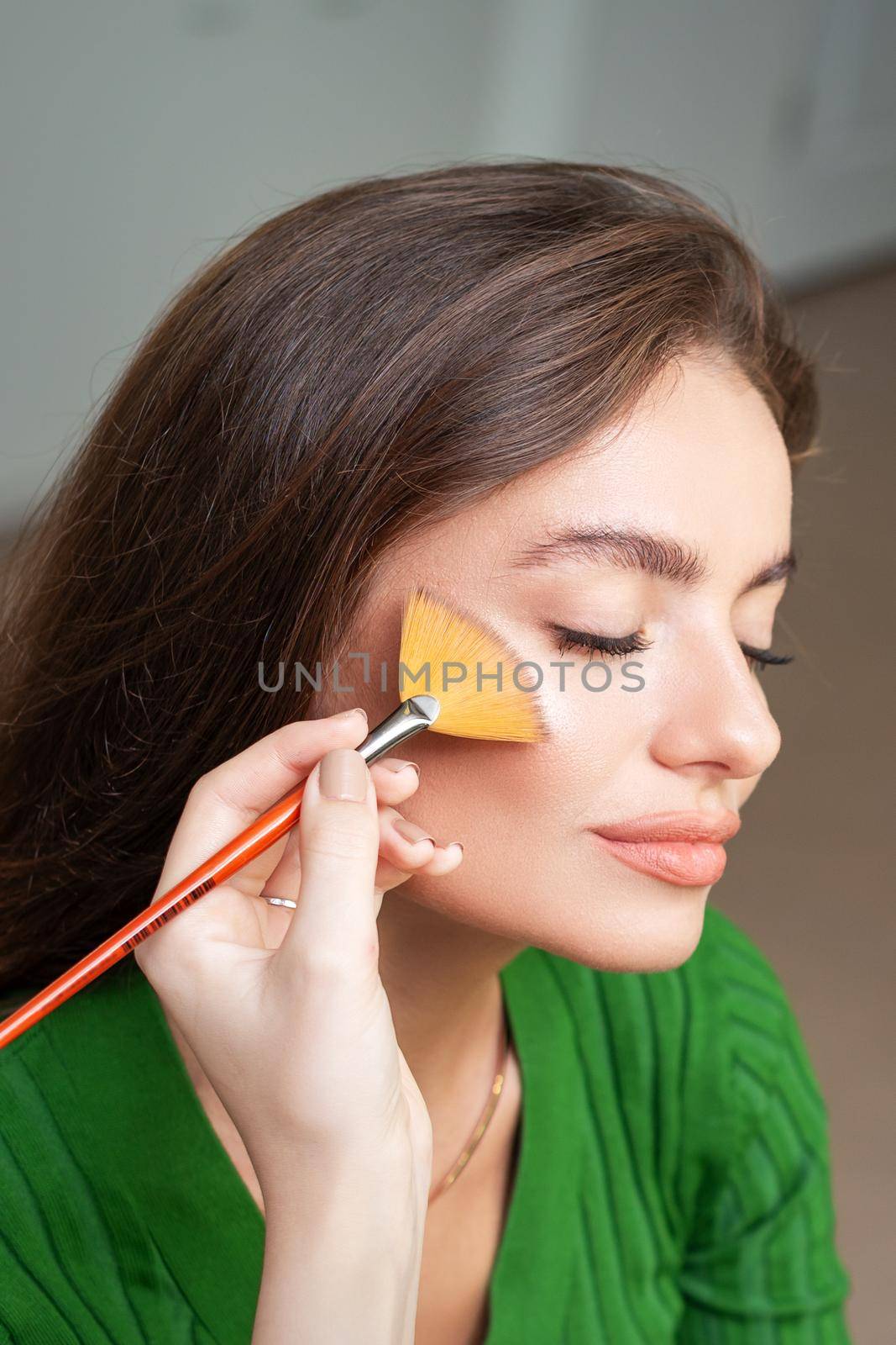 Make up artist applying professional make up of tonal foundation on the face of beautiful young caucasian woman in make up room. Base for make up.