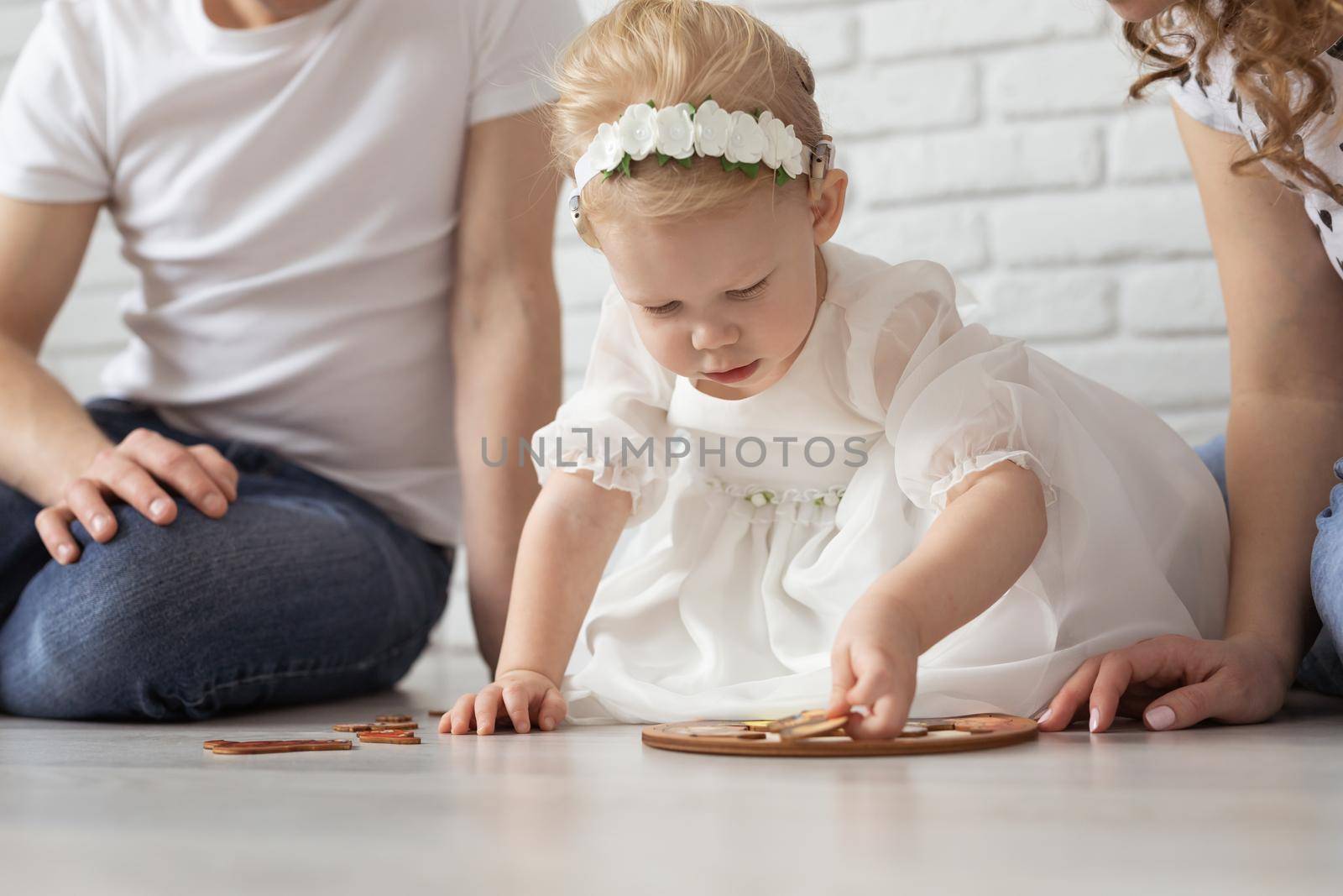 Baby child with hearing aids and cochlear implants plays with parents on floor. Deaf and rehabilitation and diversity concept by Satura86