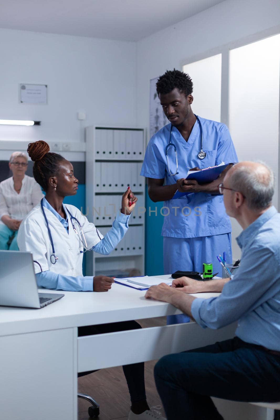 Hospital staff reviewing retired patient record file while talking about prescribed medicine. Clinic specialist discussing with nurse about consultation appointment dates.