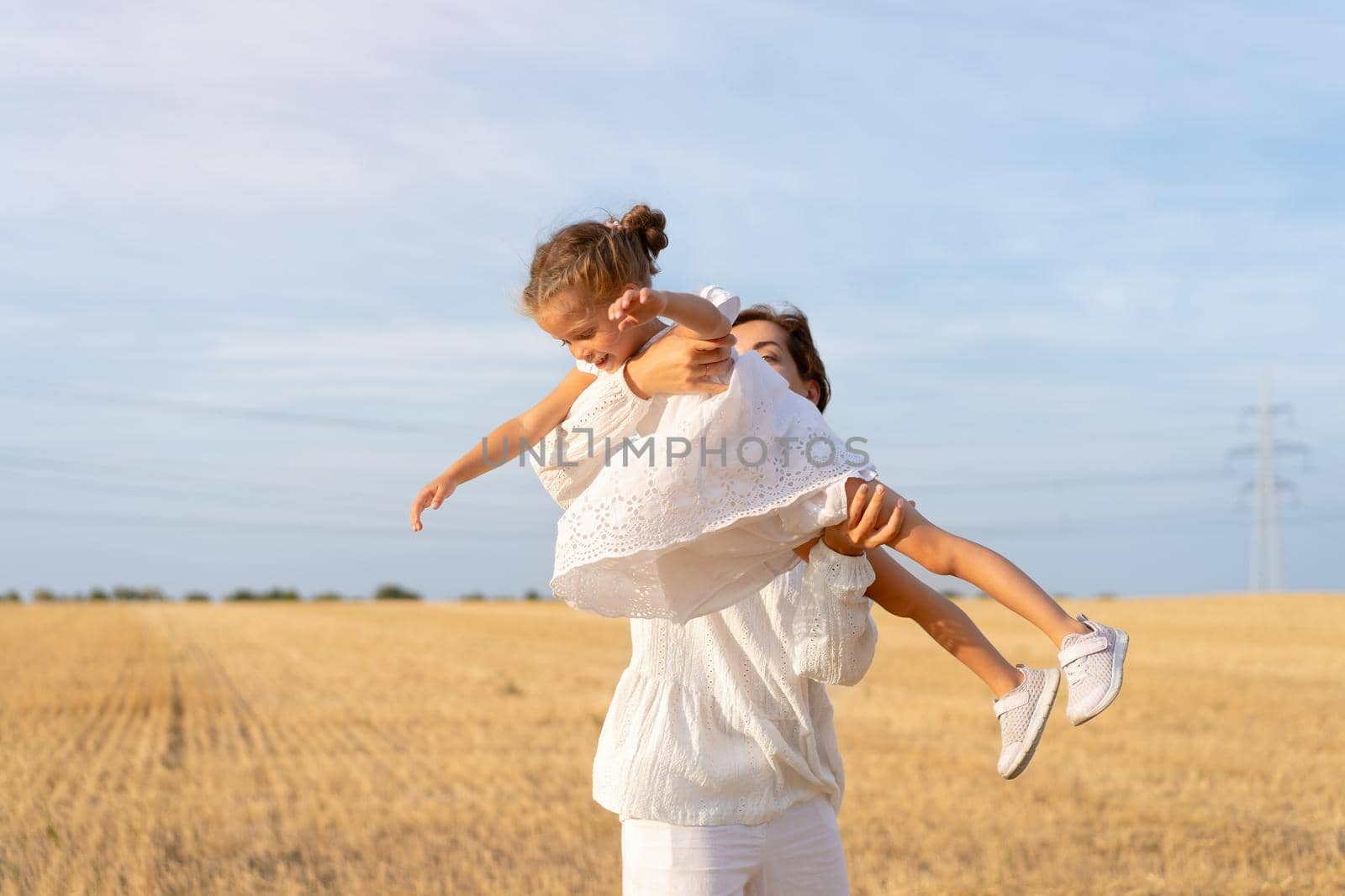 Mother throws up little daughter in air standing wheat field summer day blue sky background. Mom throw up little girl. Happy family concept. White dress. Happy childhood. 35 and 5 years female outdoor