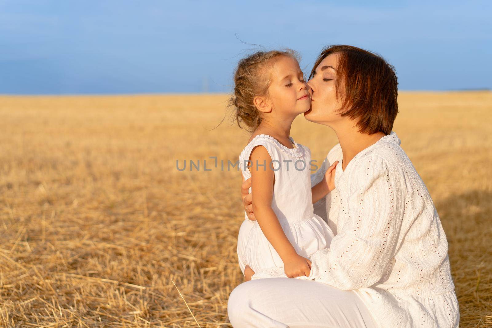 Mom kisses daughter cheek wheat field. Mother kiss little girl Happy family relationship outdoor. Dressed white. Caucasian female woman 35 years and girl 5 years old