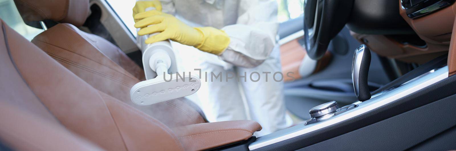 Close-up of hazmat worker cleansing car interior with spray disinfectant and steam heat. Protect car upholstery from virus. Coronavirus prevention concept