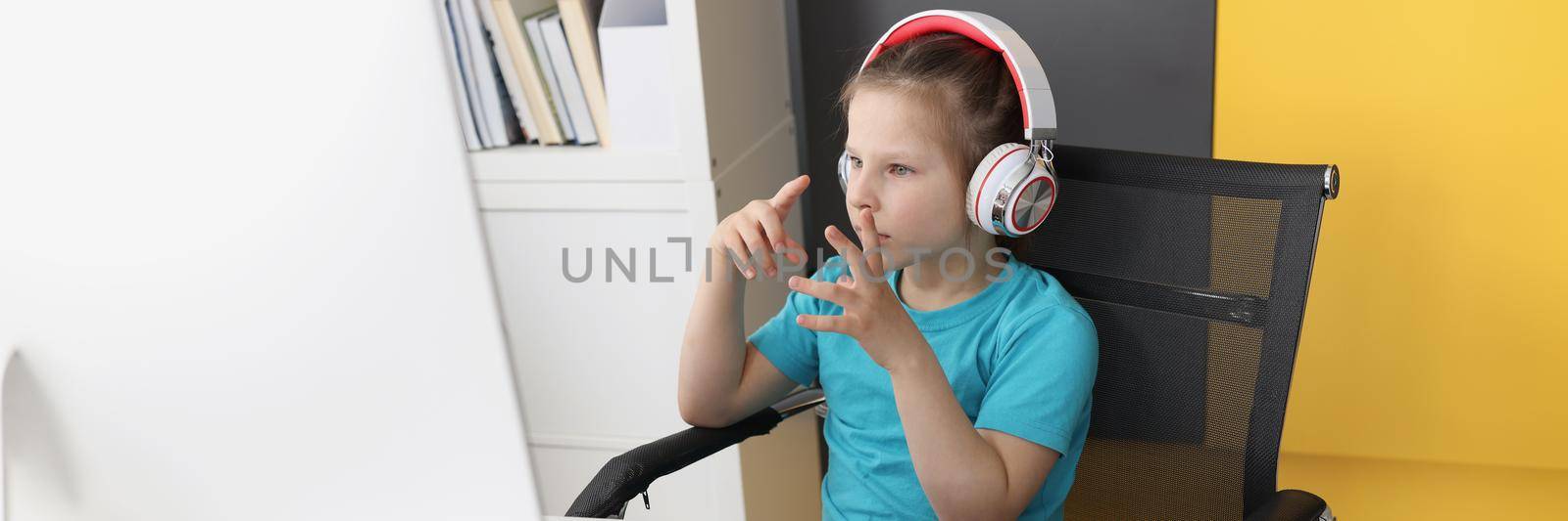 Portrait of girl having online school classes from home because of pandemic situation. Child repeat after teacher wear headset. Distance education concept