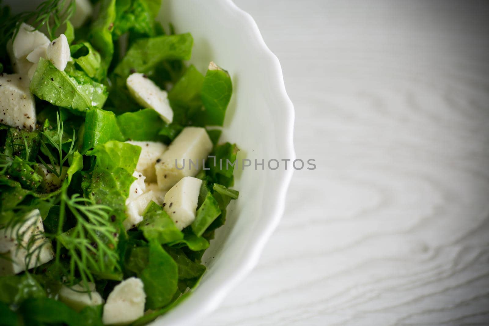fresh green lettuce salad with mozzarella and herbs in a bowl, on a wooden table