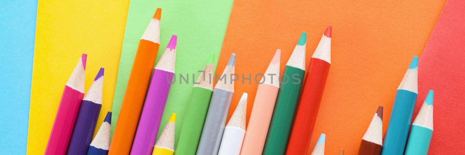 Top view of pencils collection chaotically placed on colored paper for childs art. Crayon ready to paint and create unique drawing. Creativity, art concept