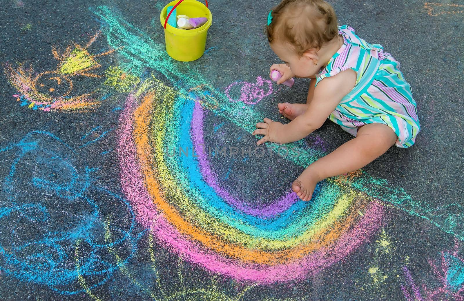Baby draws a rainbow on the pavement with chalk. Selective focus. Nature.
