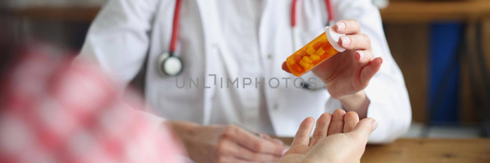 Close-up of female doctor and patient in clinic office. Physician giving to woman bottle with capsules. Hospital appointment. Medicine, treatment and healthcare concept