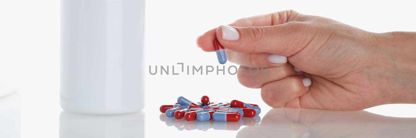 Womans hand hold one jelly capsule bunch of pill scattered on surface by kuprevich