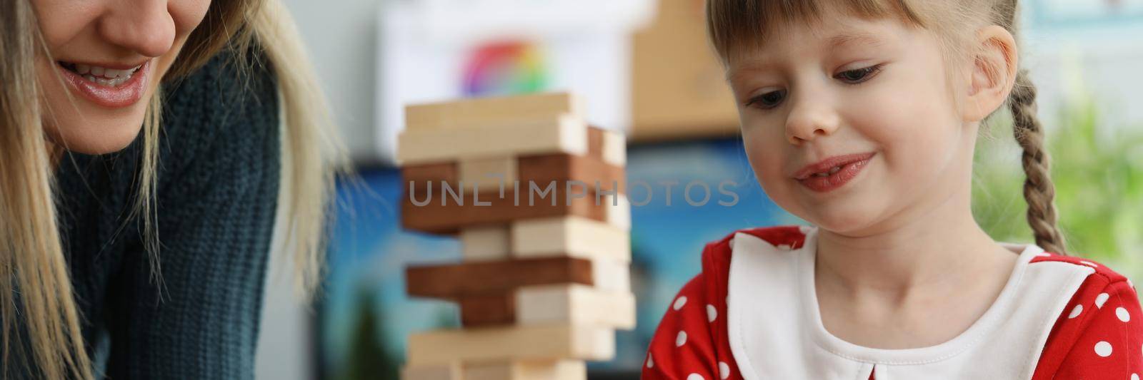 Daughter and mother spend time together playing funny wooden blocks game by kuprevich