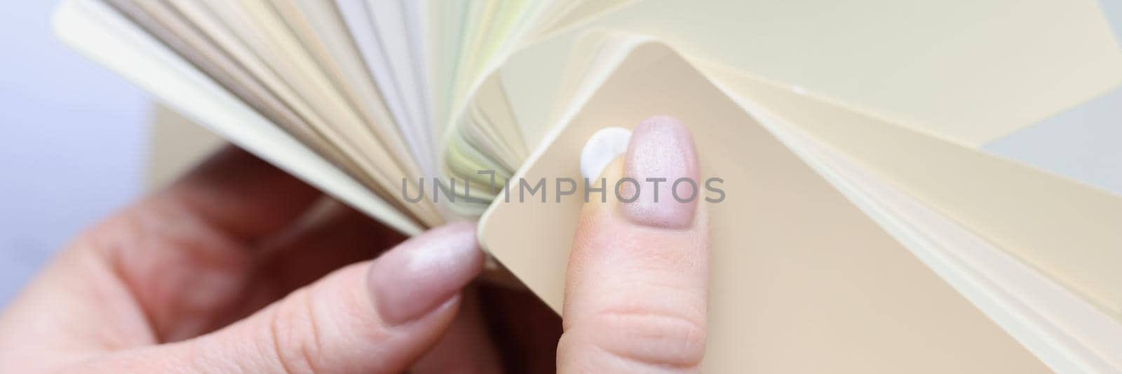 Close-up of lady graphic designer chooses colors from palette guide for painting. Samples of different shades of beige colour. Designer, creativity concept