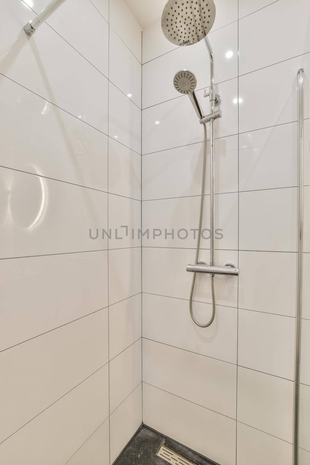 Shower faucets attached to tiled wall near glass partition and ornamental curtail in washroom at home