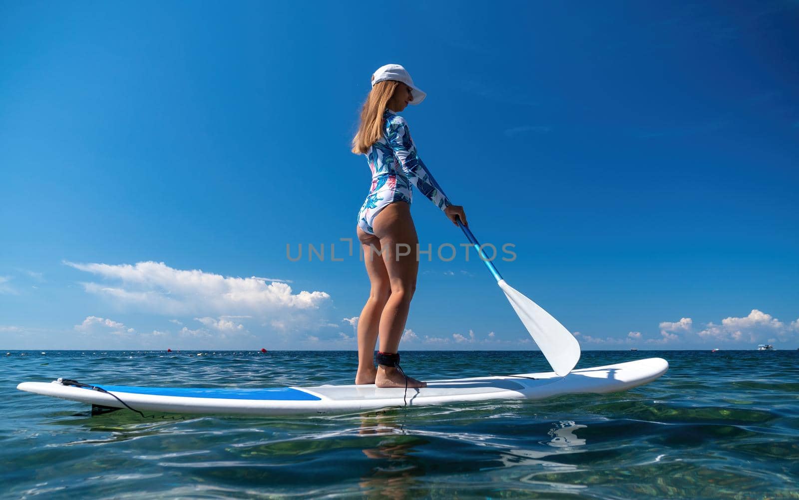 Healthy happy fit woman in bikini relaxing on a sup surfboard, floating on the clear turquoise sea water. Recreational Sports. Stand Up Paddle boarding. Summer fun, holidays travel. Active lifestyle by panophotograph