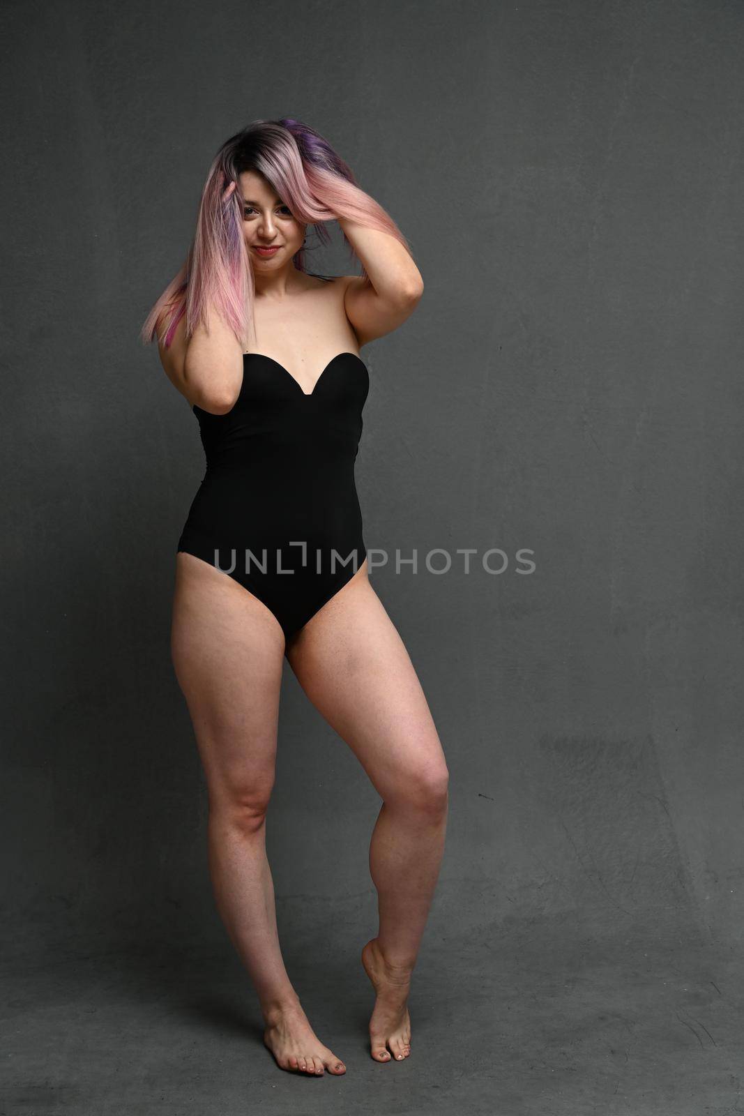 Full length adult woman in a black bodysuit holding her hair with a smile