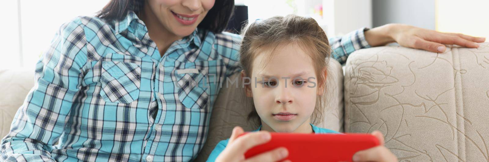 Daughter play online video games on smartphone and mum watch it by kuprevich