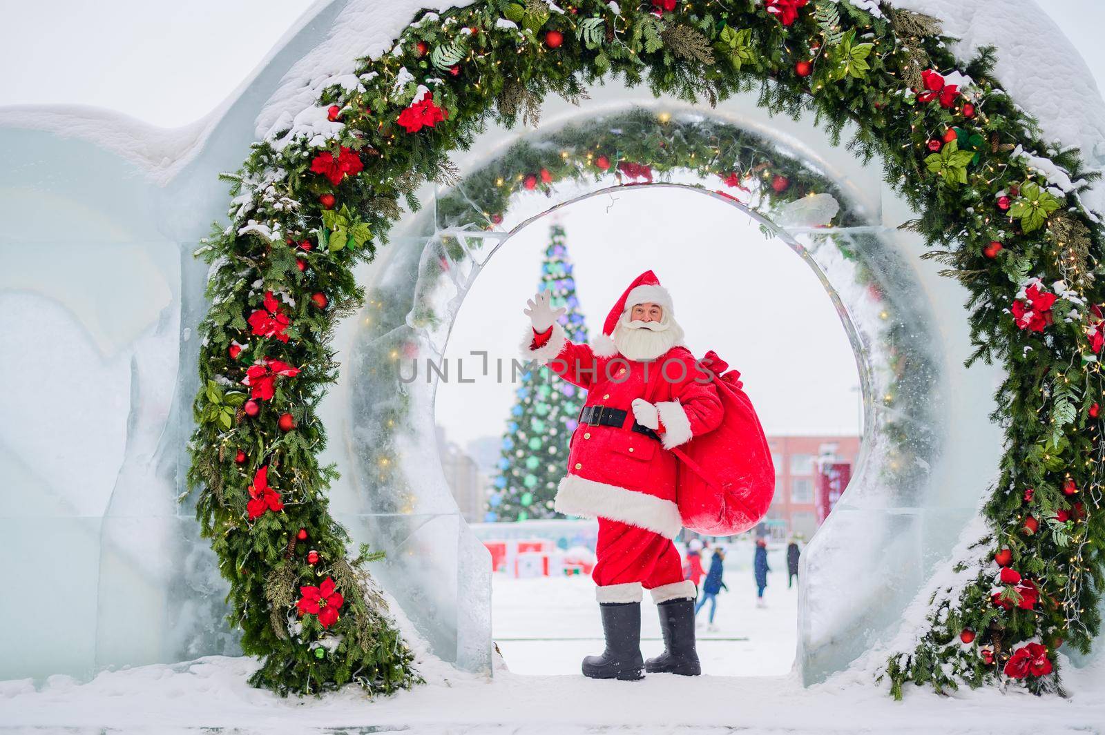 Santa Claus posing with a bag of gifts on the background of Christmas decorations outdoors.