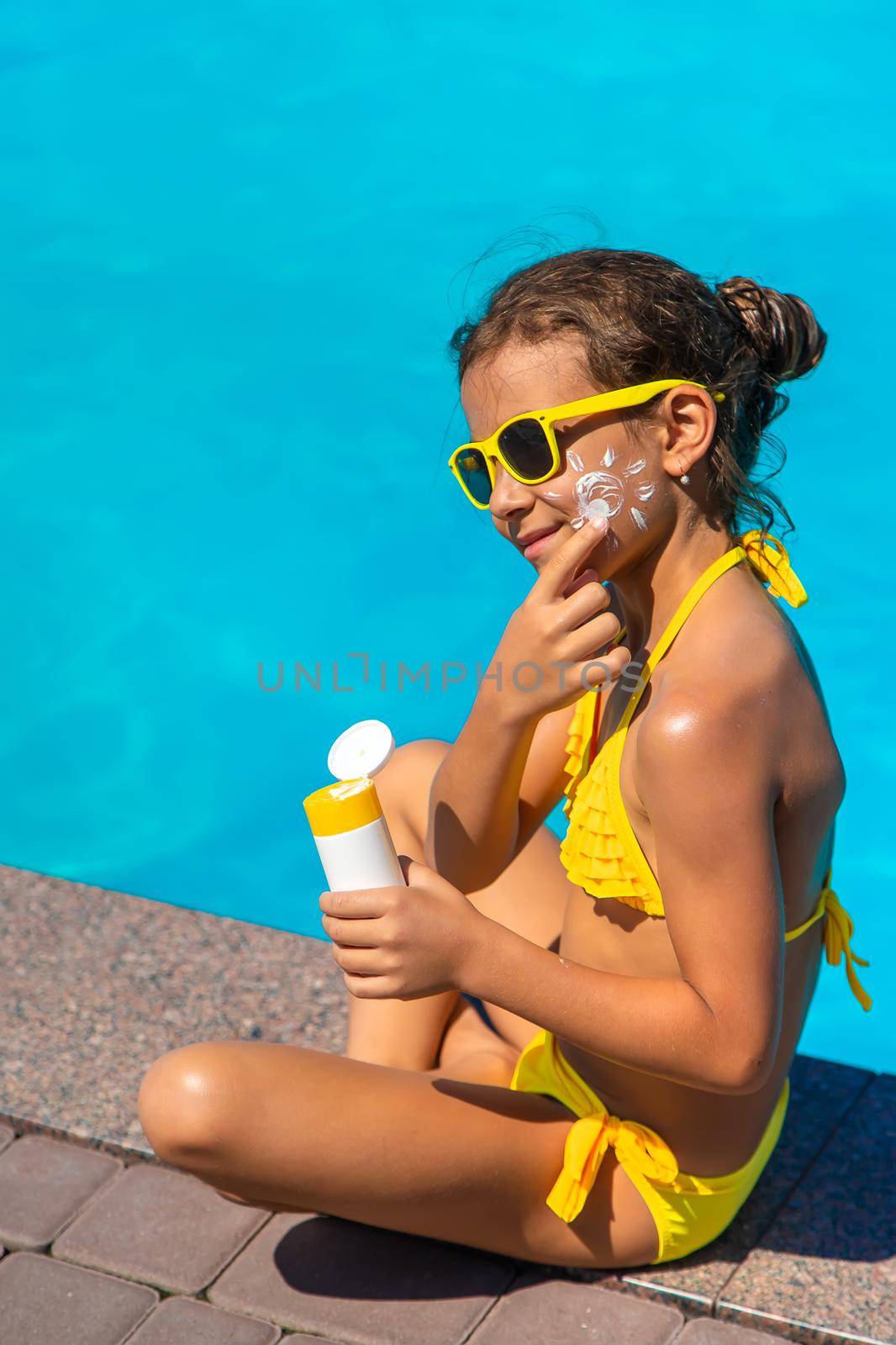 Sunscreen near the pool on the face of the child. Selective focus. by yanadjana