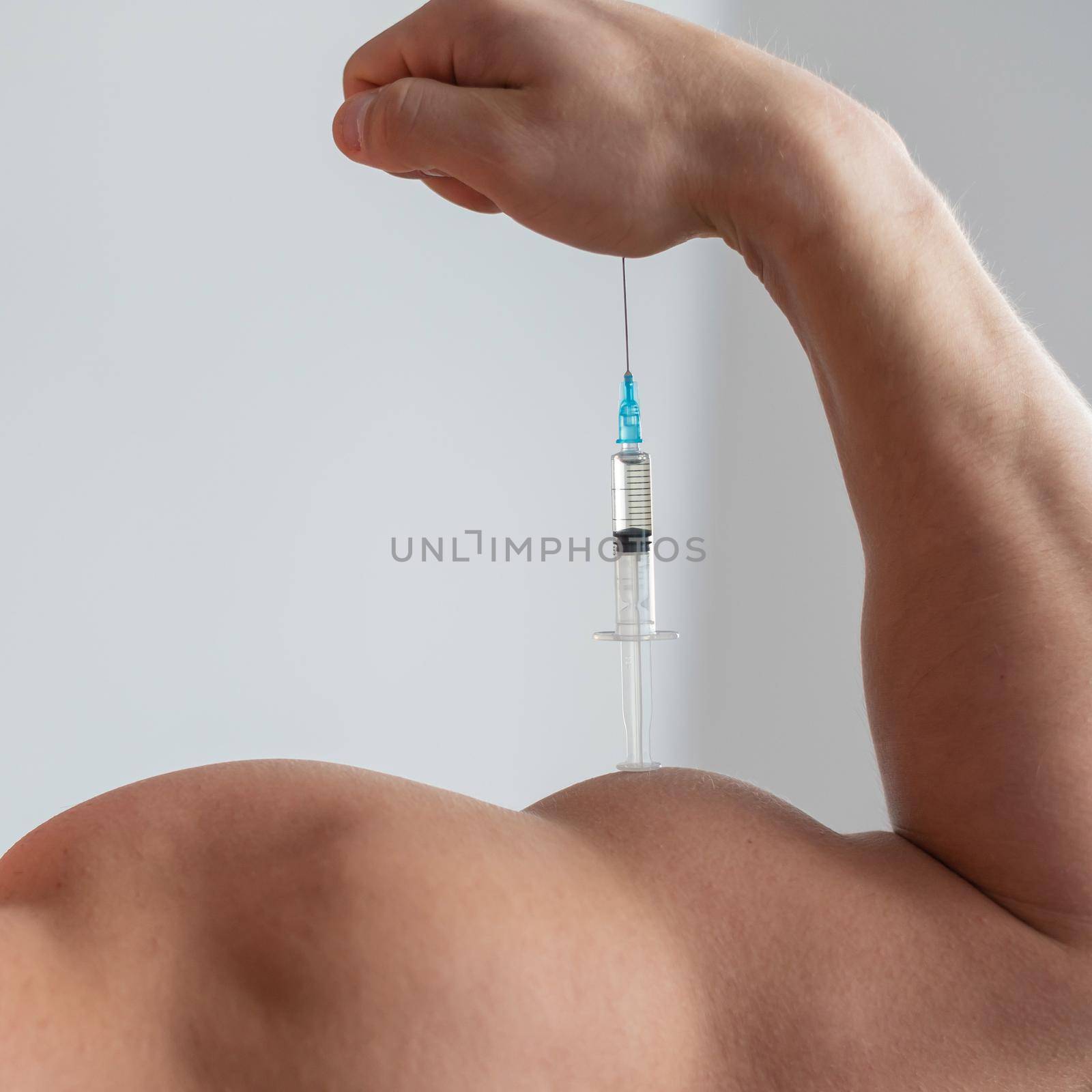 Closeup of a male hand with a dope syringe. Cropped biceps of a man. Unrecognizable bodybuilder sets himself growth hormone testosterone. by mrwed54