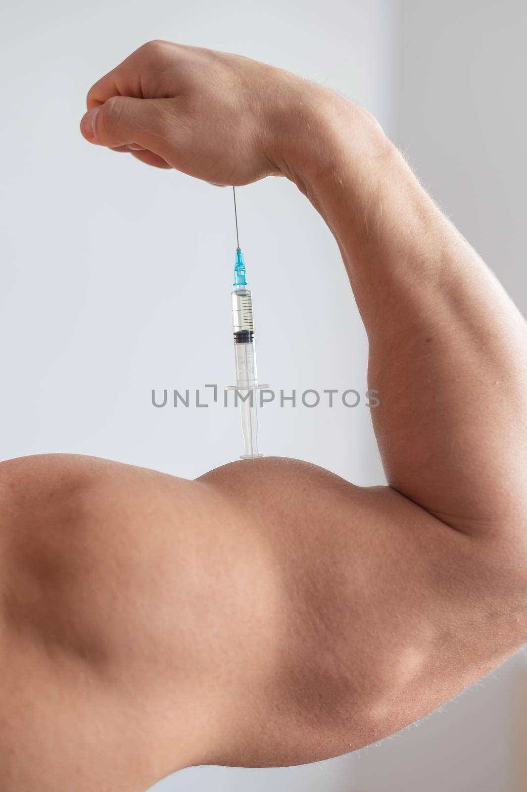 Closeup of a male hand with a dope syringe. Cropped biceps of a man. Unrecognizable bodybuilder sets himself growth hormone testosterone. Vertical photo. by mrwed54