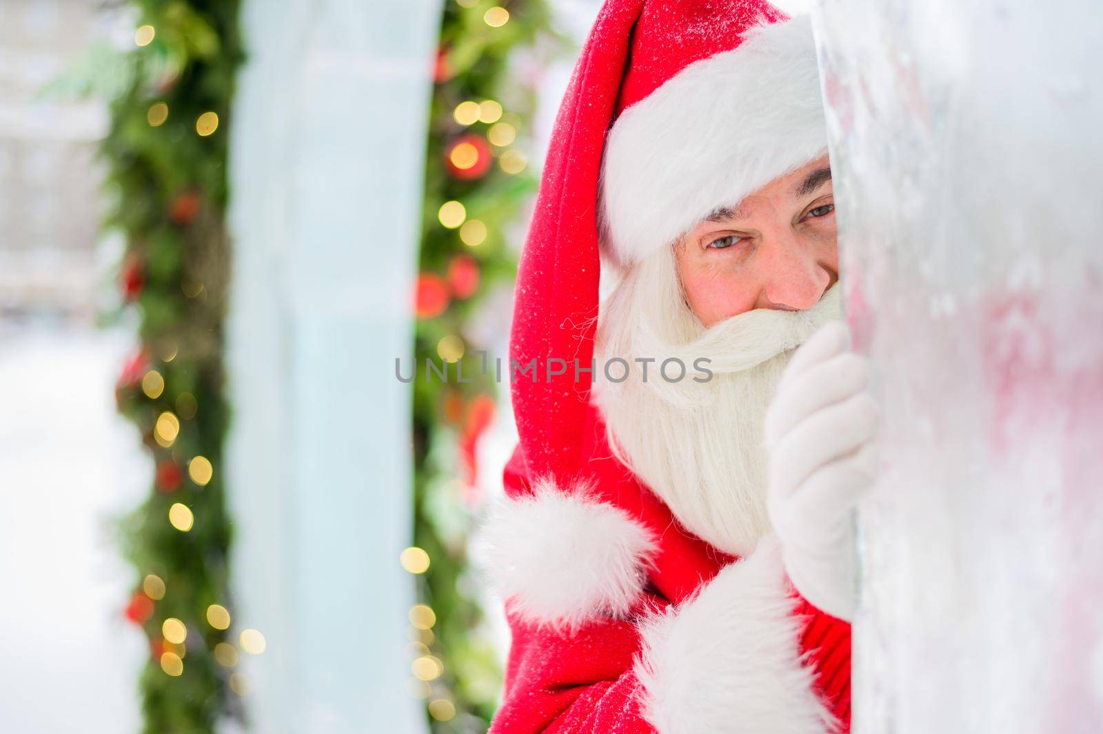 Santa claus peeks out of Christmas decorations outdoors.