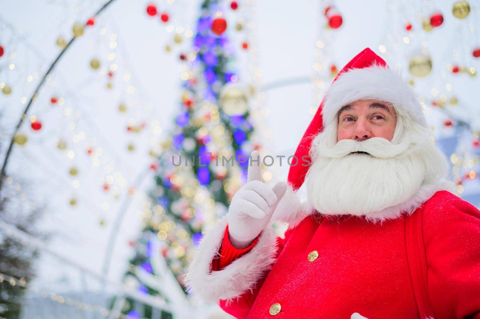 Portrait of an elderly man dressed as santa claus on the background of a christmas tree outdoors
