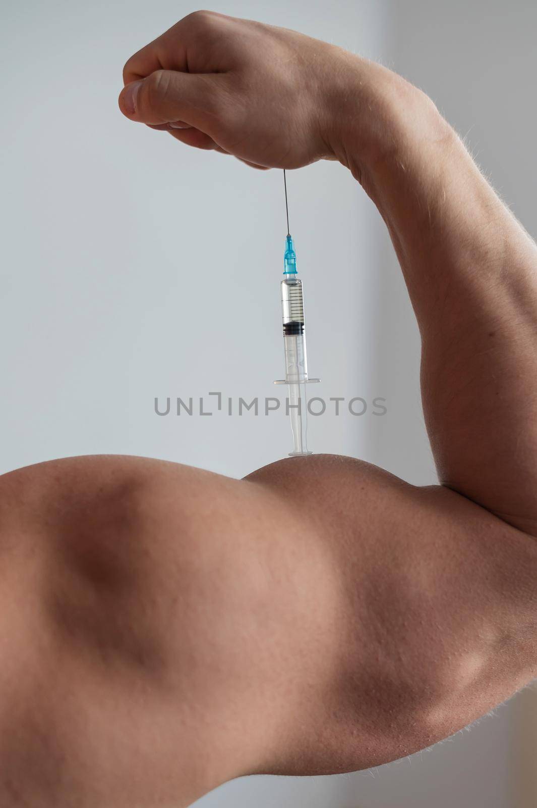Closeup of a male hand with a dope syringe. Cropped biceps of a man. Unrecognizable bodybuilder sets himself growth hormone testosterone. Vertical photo. by mrwed54