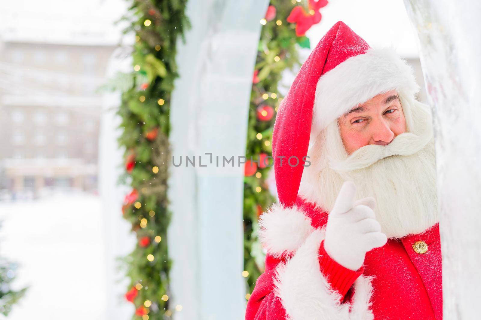 Santa claus peeks out of Christmas decorations outdoors.