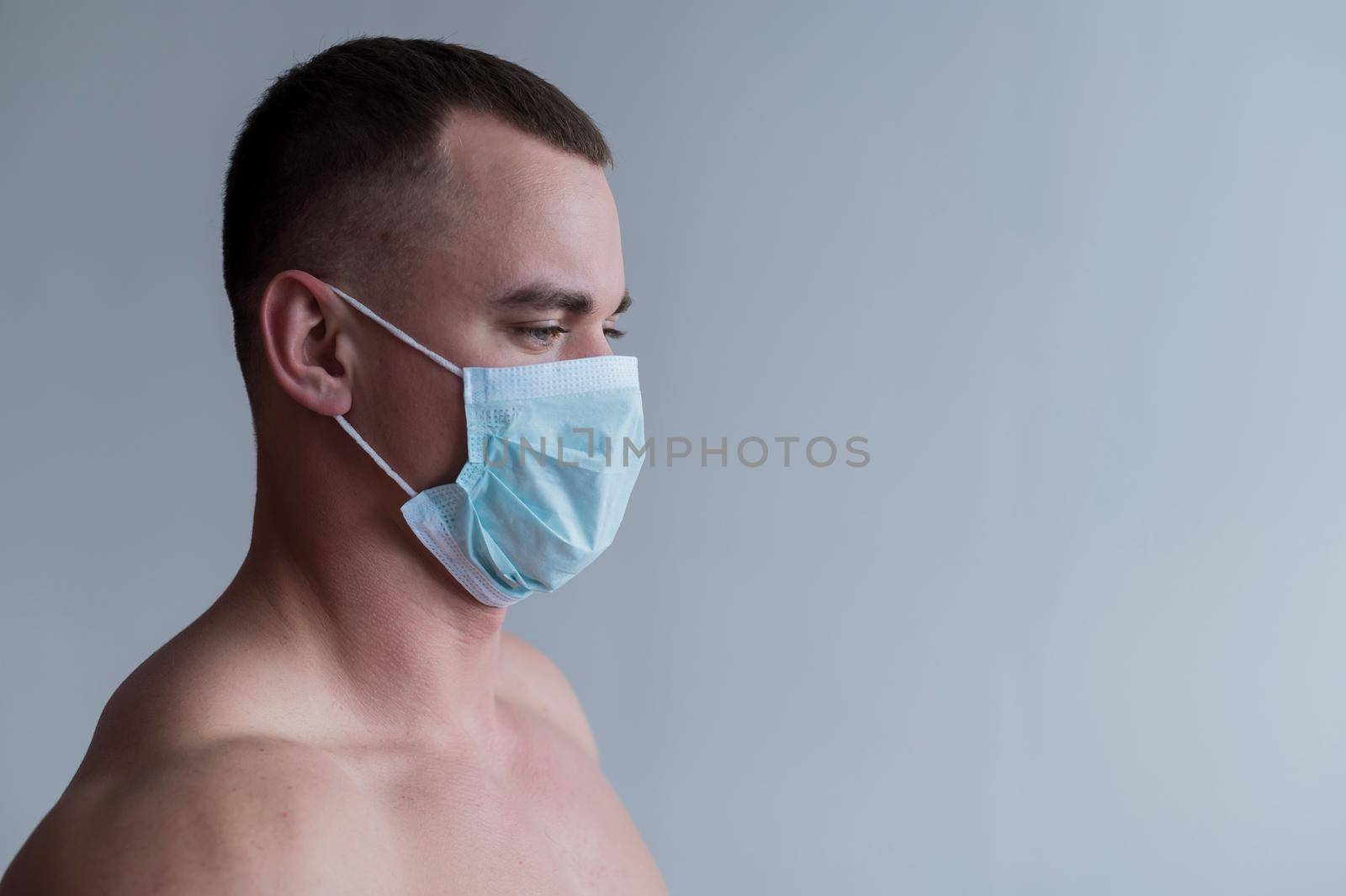 A male bodybuilder in a medical mask crossed his arms over his muscular bare chest. The guy goes in for sports in quarantine. Respiratory protection