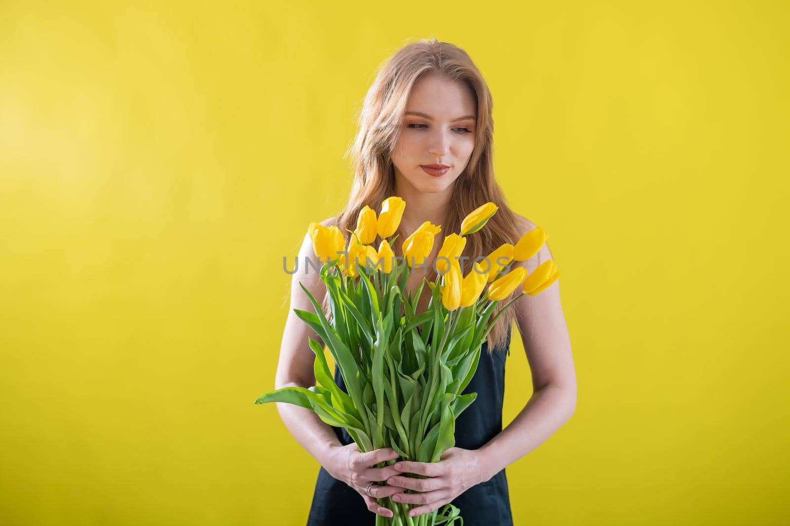 Caucasian woman with an armful of yellow tulips on a yellow background. International Women's Day. Bouquet of spring flowers by mrwed54