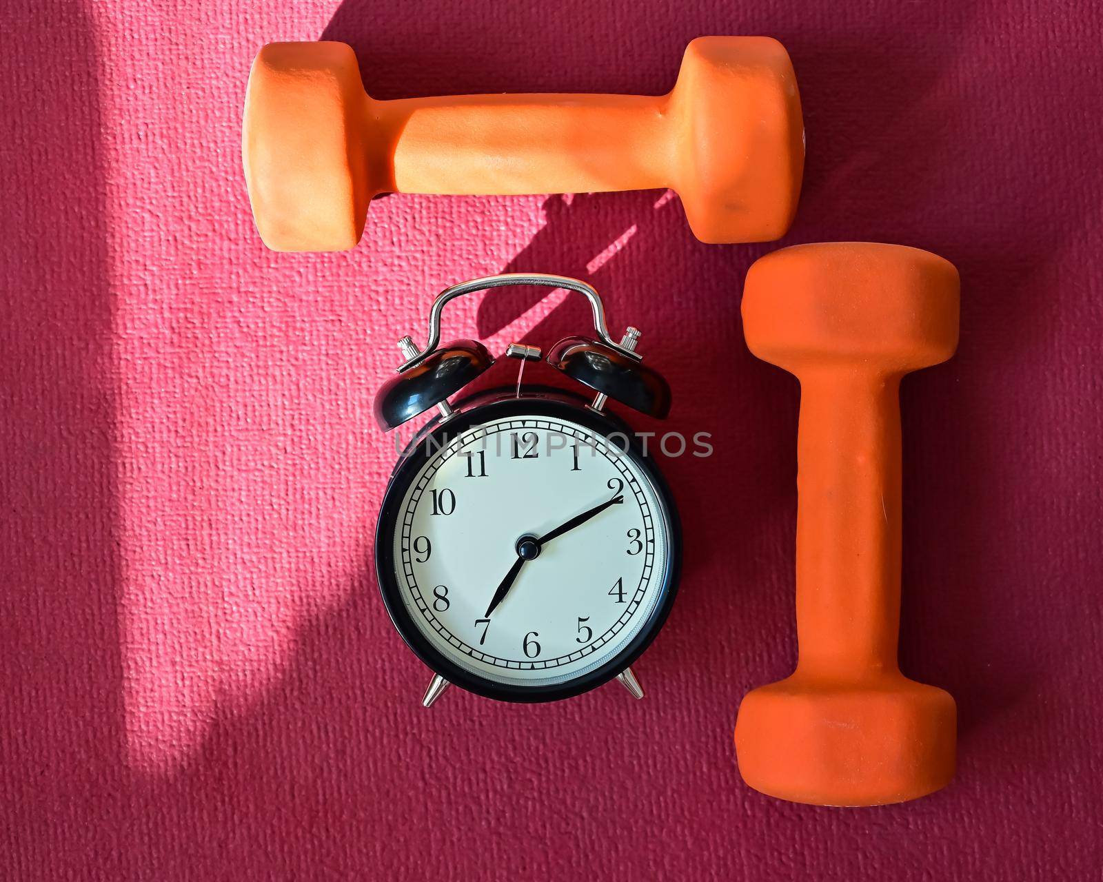 Two orange tunnels and an alarm clock on a pink yoga mat. Time to do fitness at home with equipment. Quarantine sports discipline.