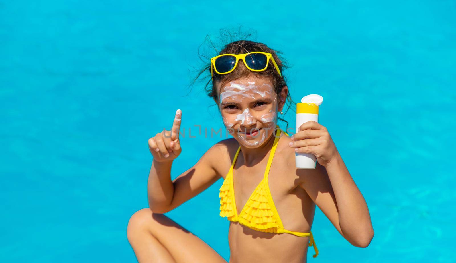 Sunscreen near the pool on the face of the child. Selective focus. by yanadjana