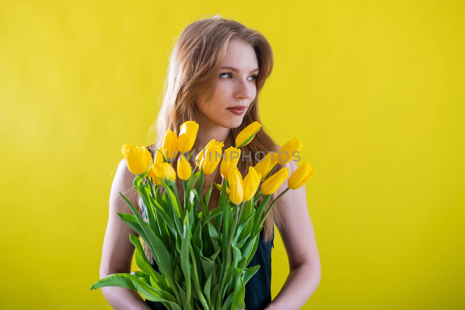 Caucasian woman with an armful of yellow tulips on a yellow background. International Women's Day. Bouquet of spring flowers by mrwed54