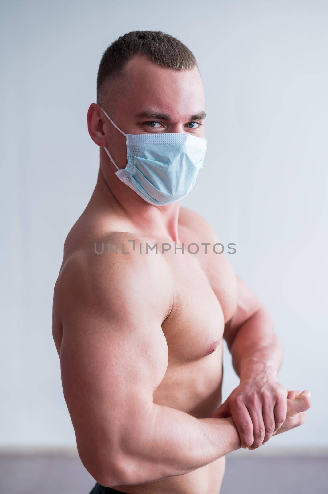 Bodybuilder with a naked torso in a medical mask. Muscular quarantine goes in for sports in quarantine. Respiratory protection. by mrwed54